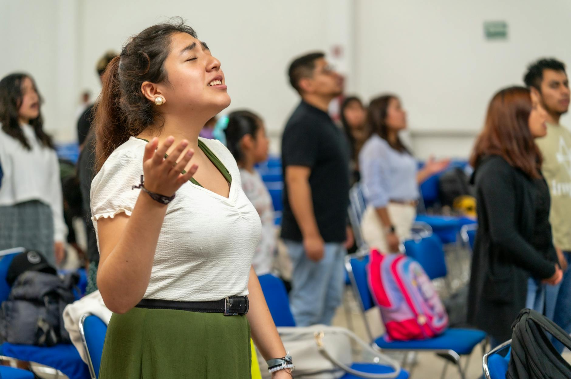 Młodzi dorośli z uniesionymi rękami na modlitewnym spotkaniu w sali