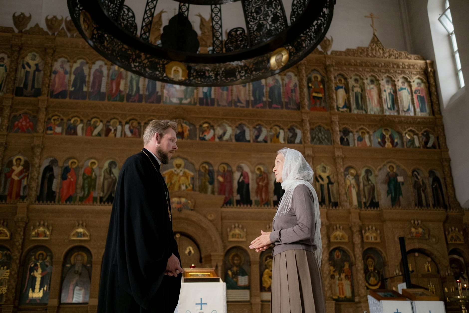 Rozmowa księdza z parafianką w bogato zdobionym cerkiewnym wnętrzu
