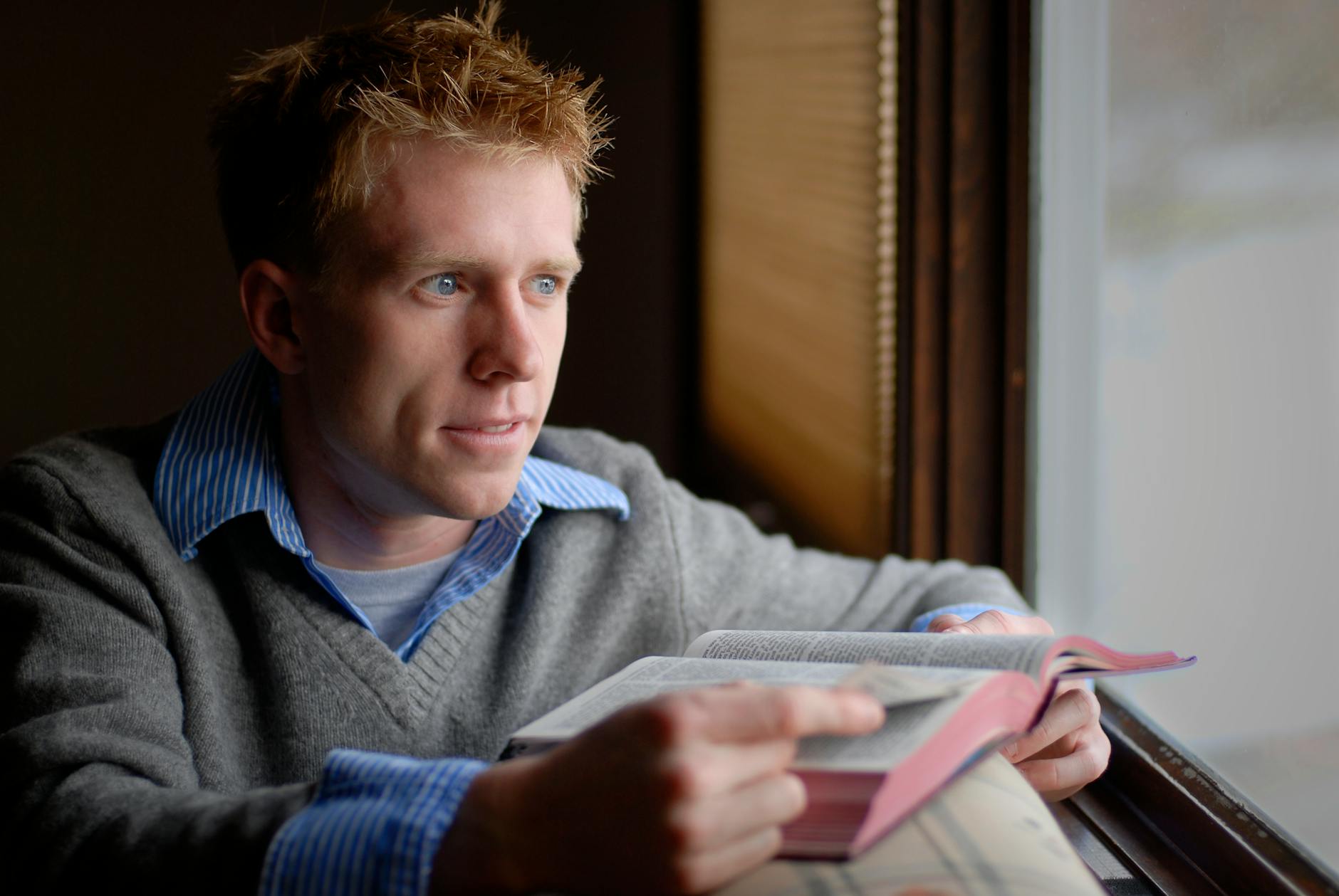 Zadumany mężczyzna czyta Biblię przy oknie