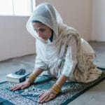 Zazdrość, pycha, lenistwo: jak rozpoznać grzechy główne w sobie? Kobieta w chuście klęczy na modlitewnym dywanie w skupieniu