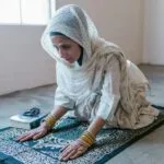 Kobieta w chuście klęczy na modlitewnym dywanie w skupieniu