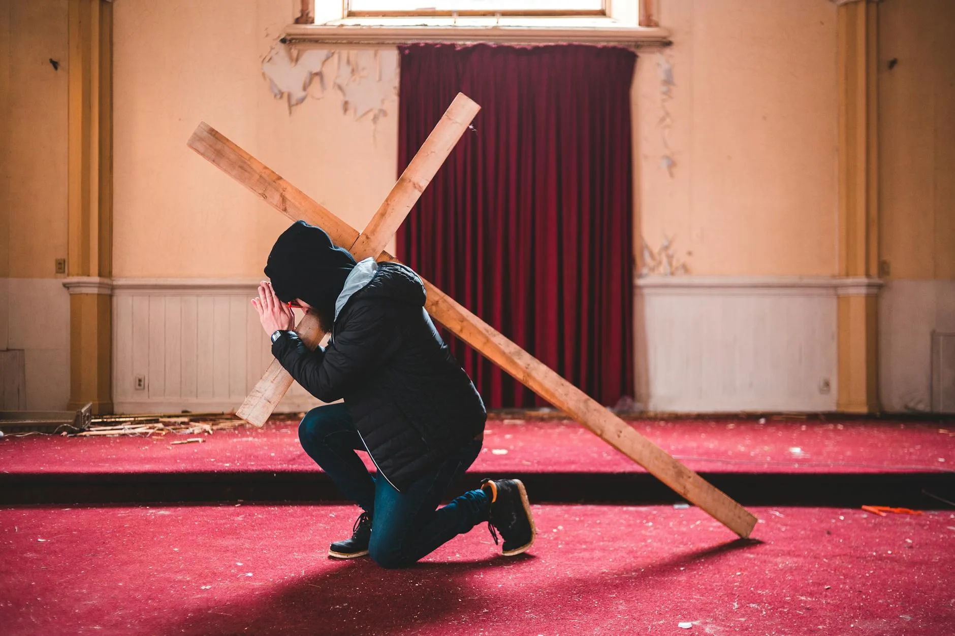 Klęcząca osoba z drewnianym krzyżem w opuszczonej kaplicy