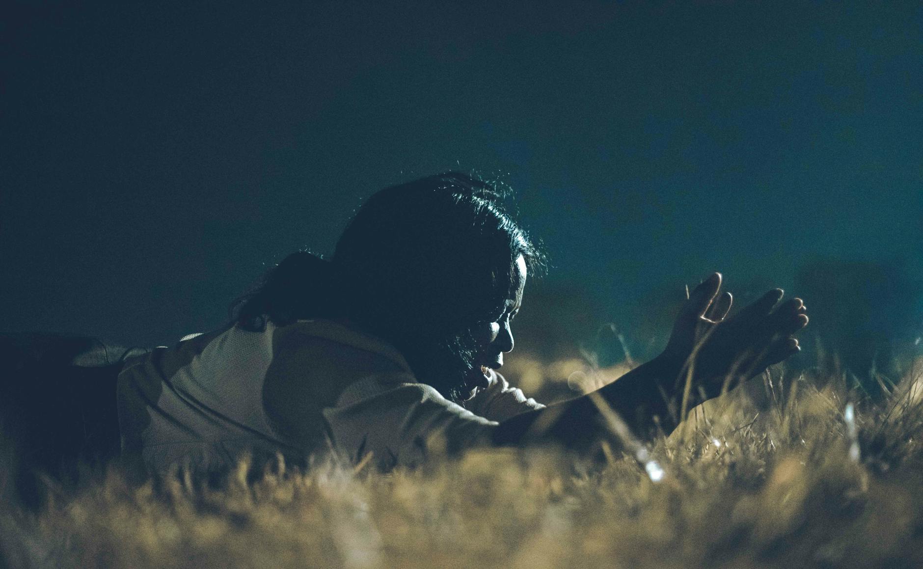 Kobieta klęczy nocą na suchej trawie, modląc się w kryzysie wiary