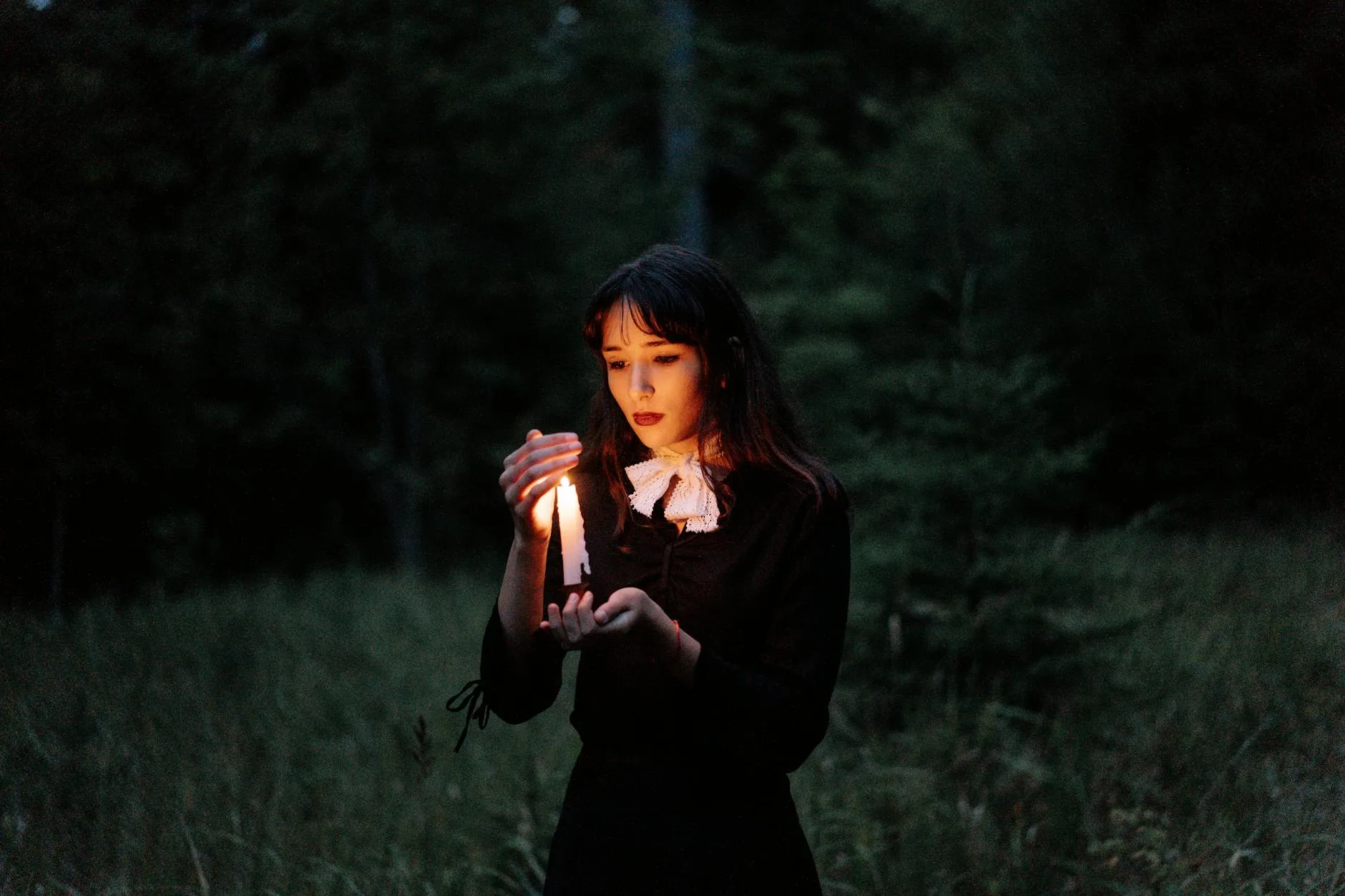 Młoda kobieta z zapaloną świecą idzie przez ciemny las