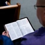 Dlaczego w liturgii czyta się Stary Testament i jak łączy się z Ewangelią? Osoba czyta Biblię w ławce kościelnej podczas modlitwy